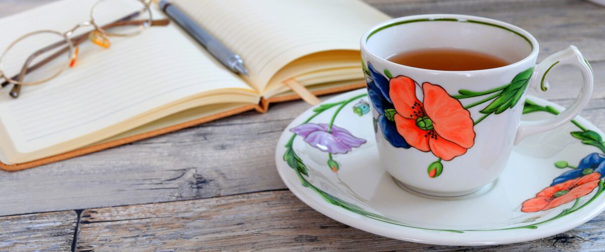 ノートと花柄カップの紅茶のあるデスク